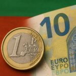 Close-up of a one Euro coin placed in front of a blurred ten Euro banknote, with the green, white, and red colors of the Bulgarian flag in the background.