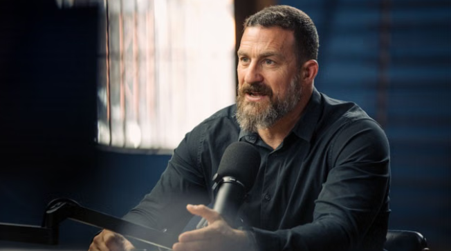 Andrew Huberman speaking into a microphone during his podcast, 2025