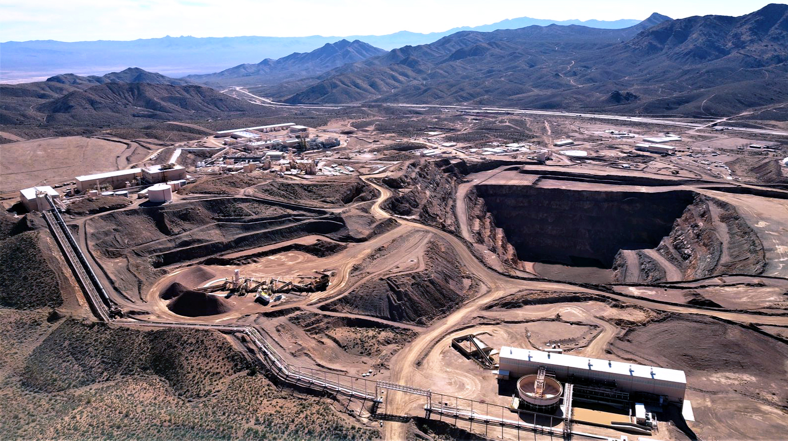 Aerial view of a large rare earth mining site surrounded by desert terrain and refining facilities, symbolizing the industrial scale and environmental challenge of mineral extraction